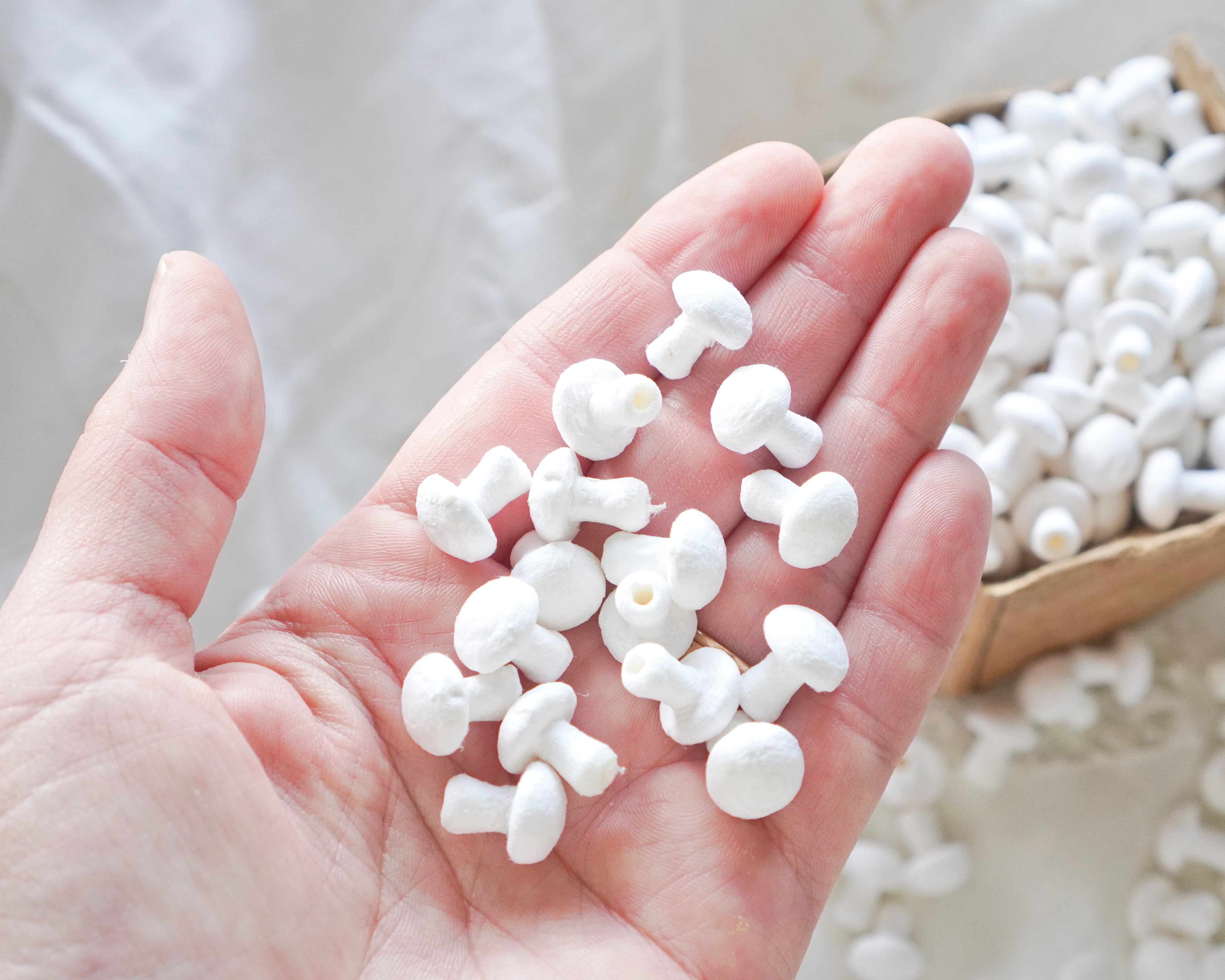 Hand holding small white craft mushrooms with a box of mushrooms in the background.