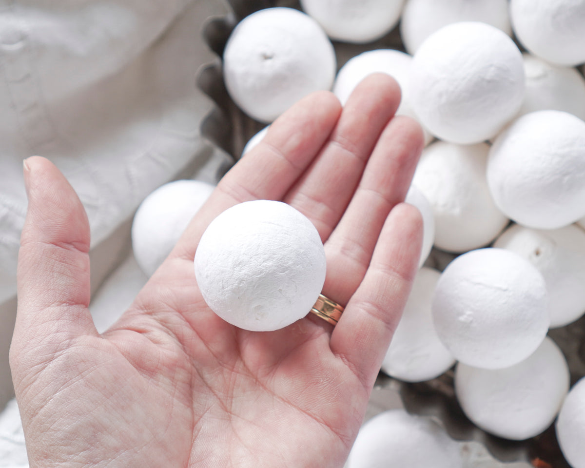A hand holds a spun cotton ball with more craft shapes in the background.