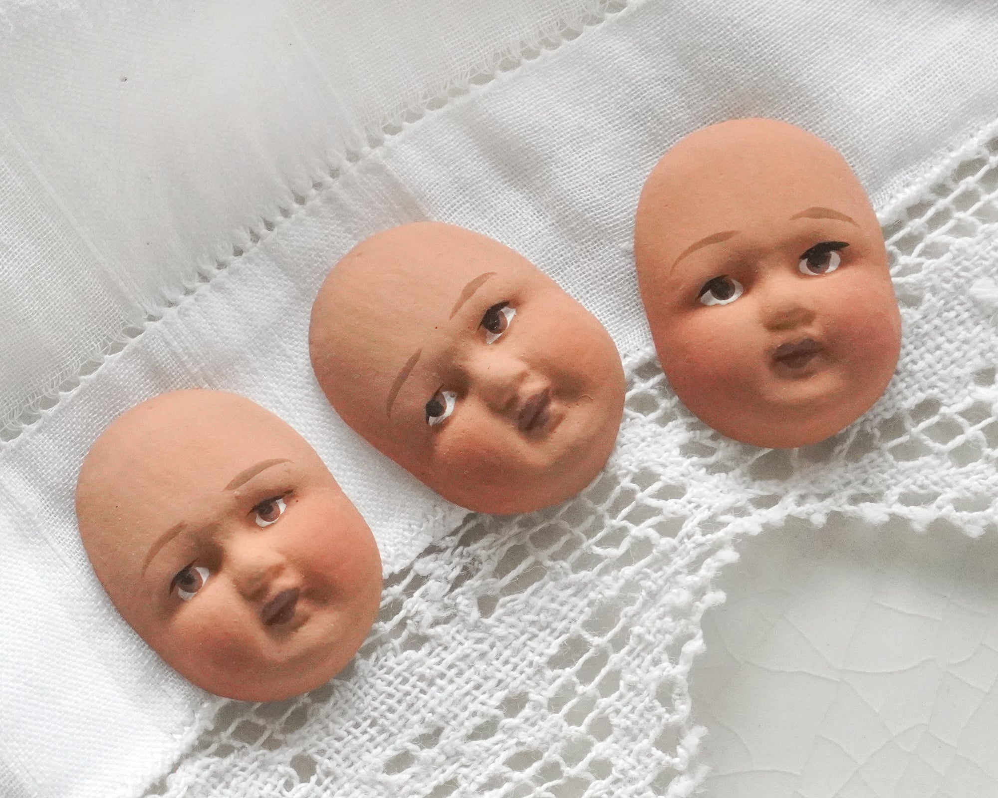 Three antique style doll heads on a white lace background