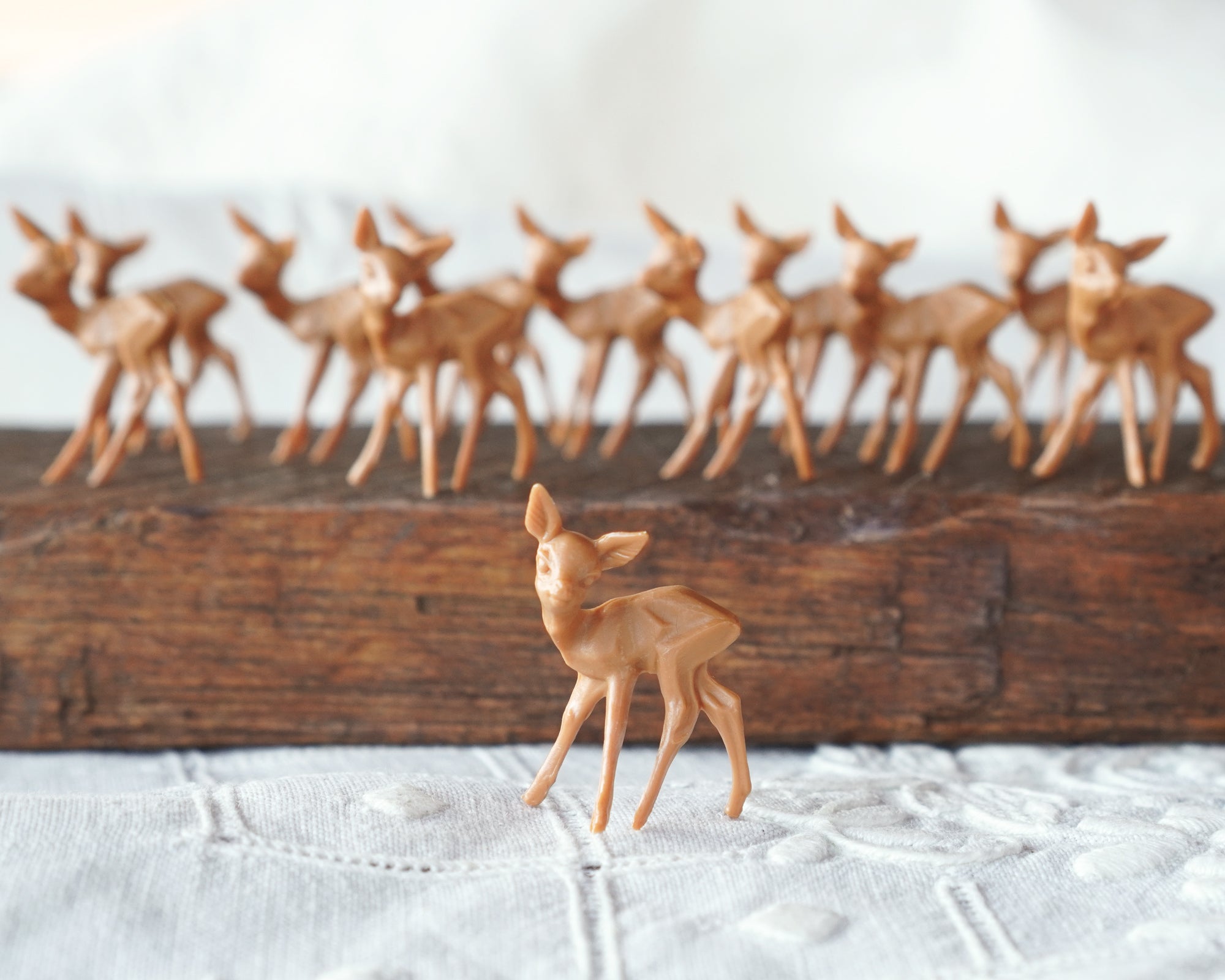 A miniature plastic deer figurine displayed in front of a group of similar figurines arranged on a wooden surface.
