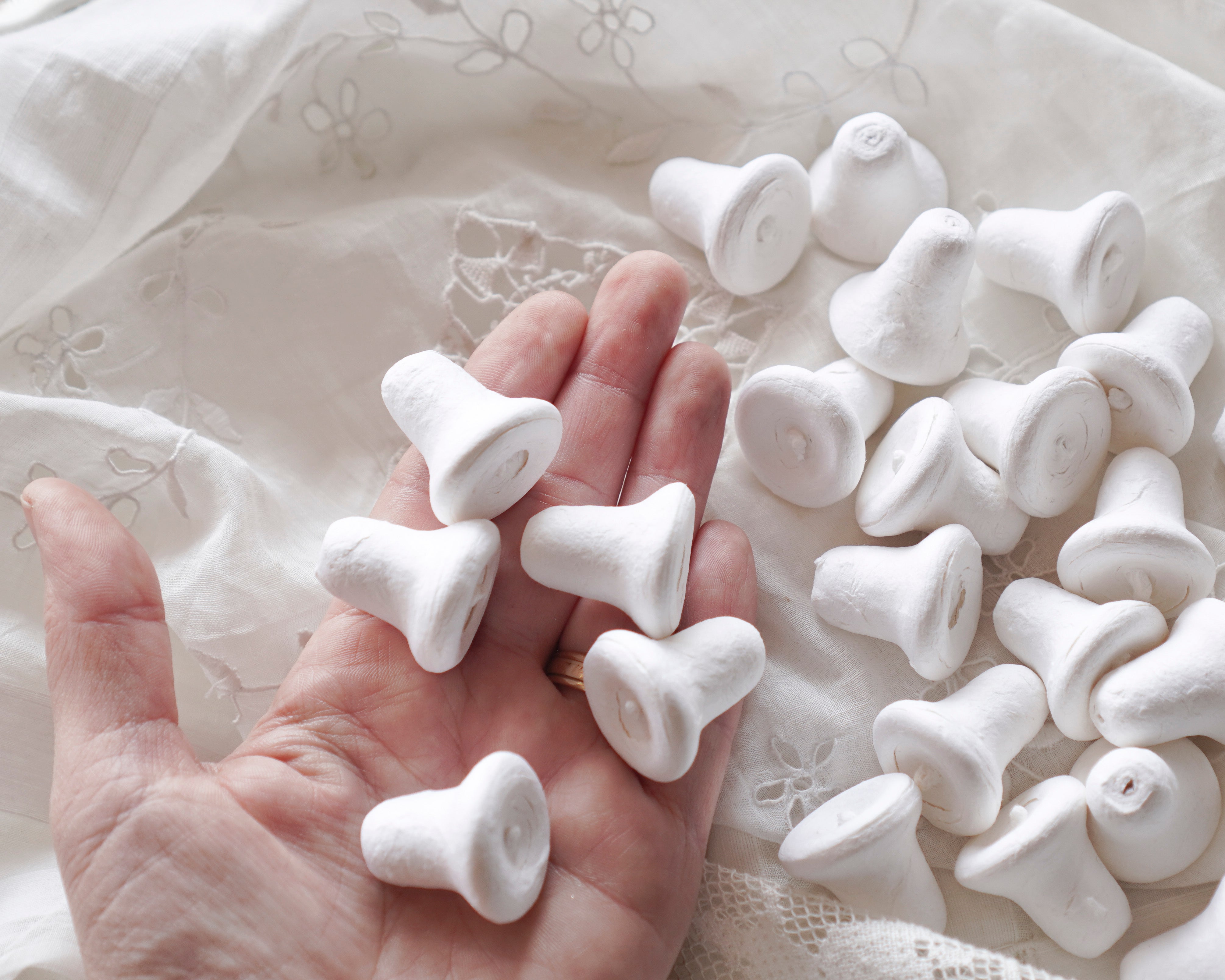 A hand holding several small white spun cotton bells, with more of the same scattered on a white lace fabric background.