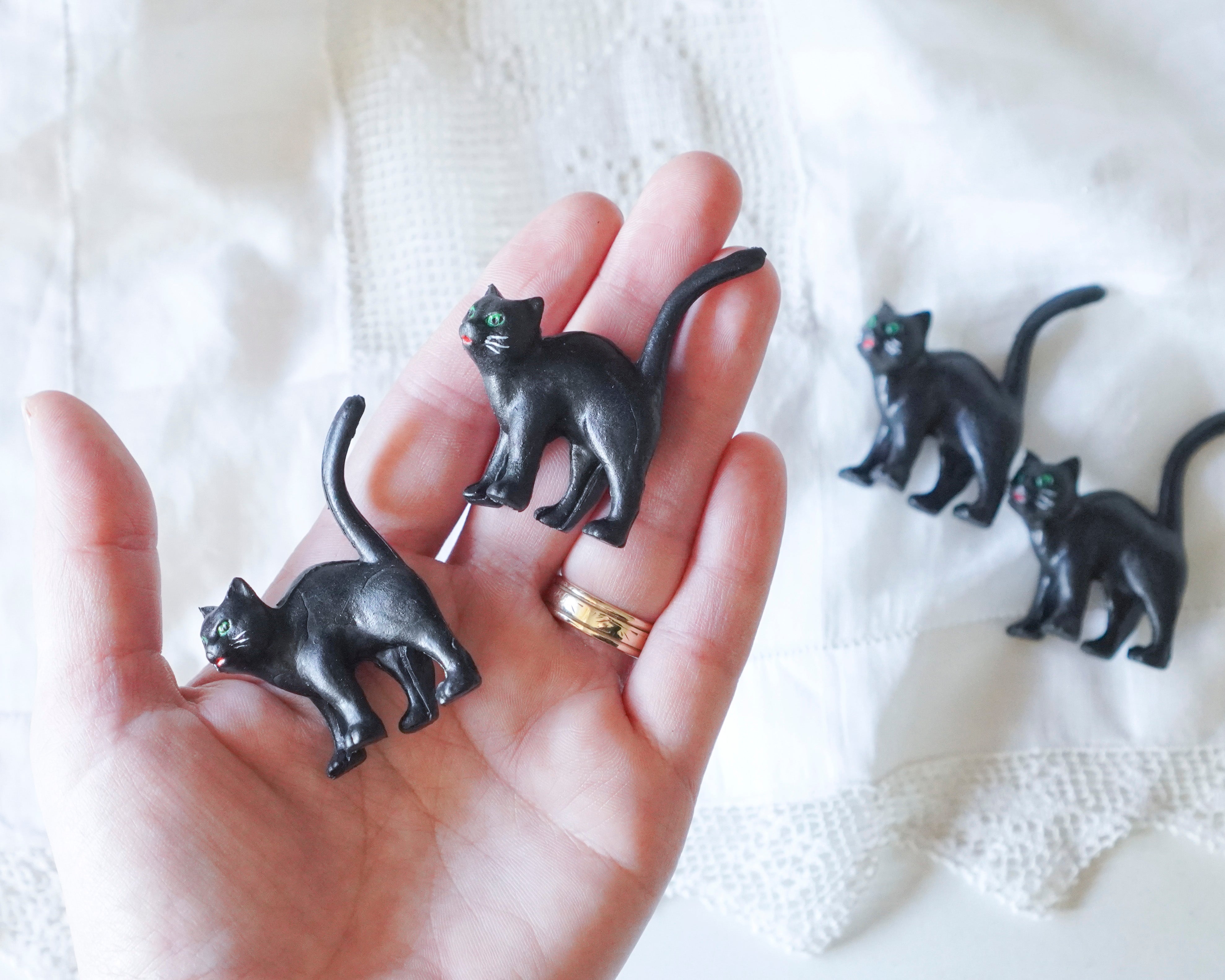 Black cat-shaped figurines held in a hand on a white textured background