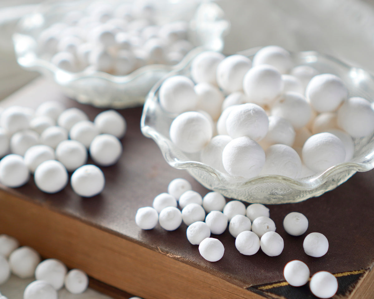 mixed size spun cotton balls displayed in bowls on a book.
