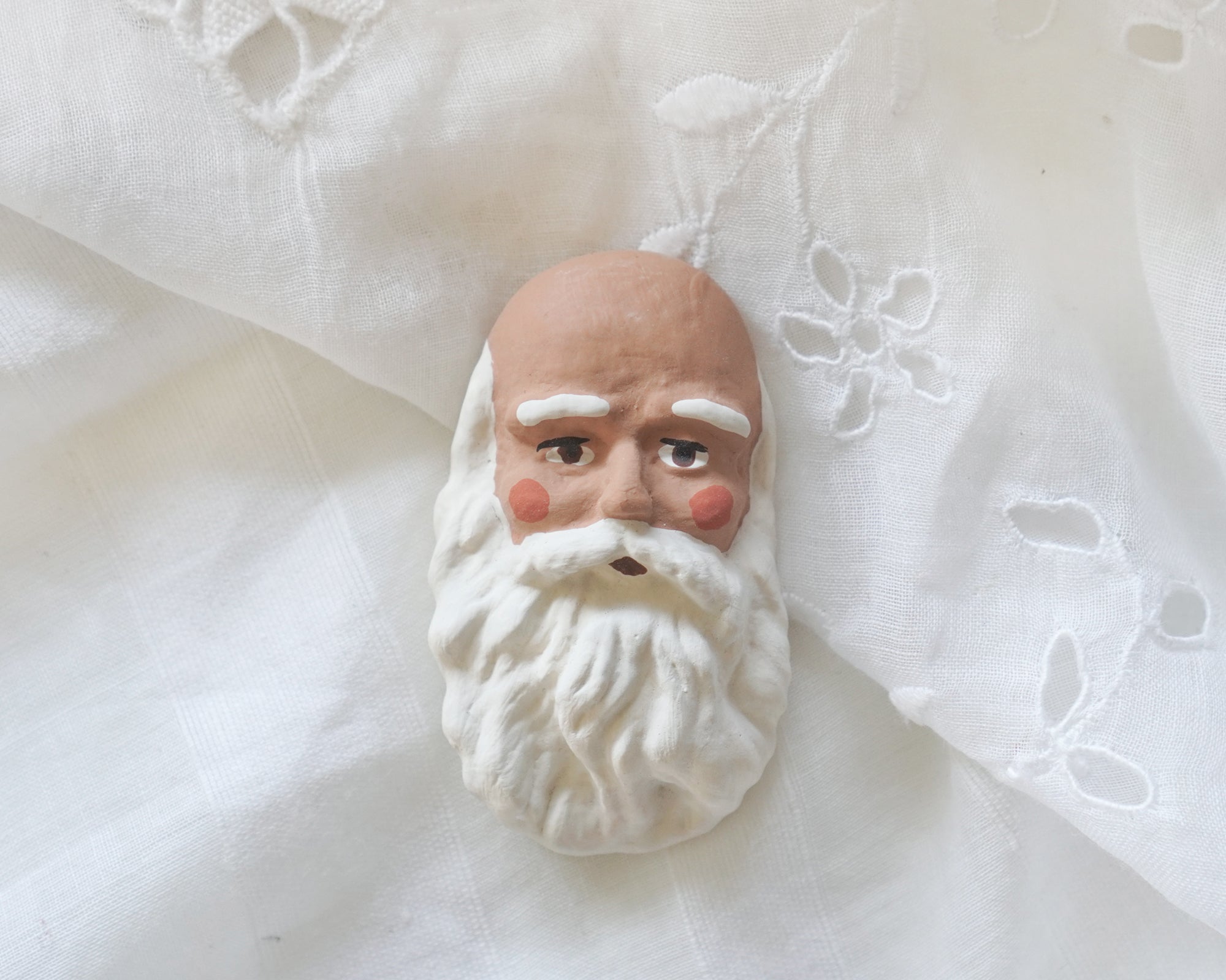 An African American Black Santa doll face on a white lace background.