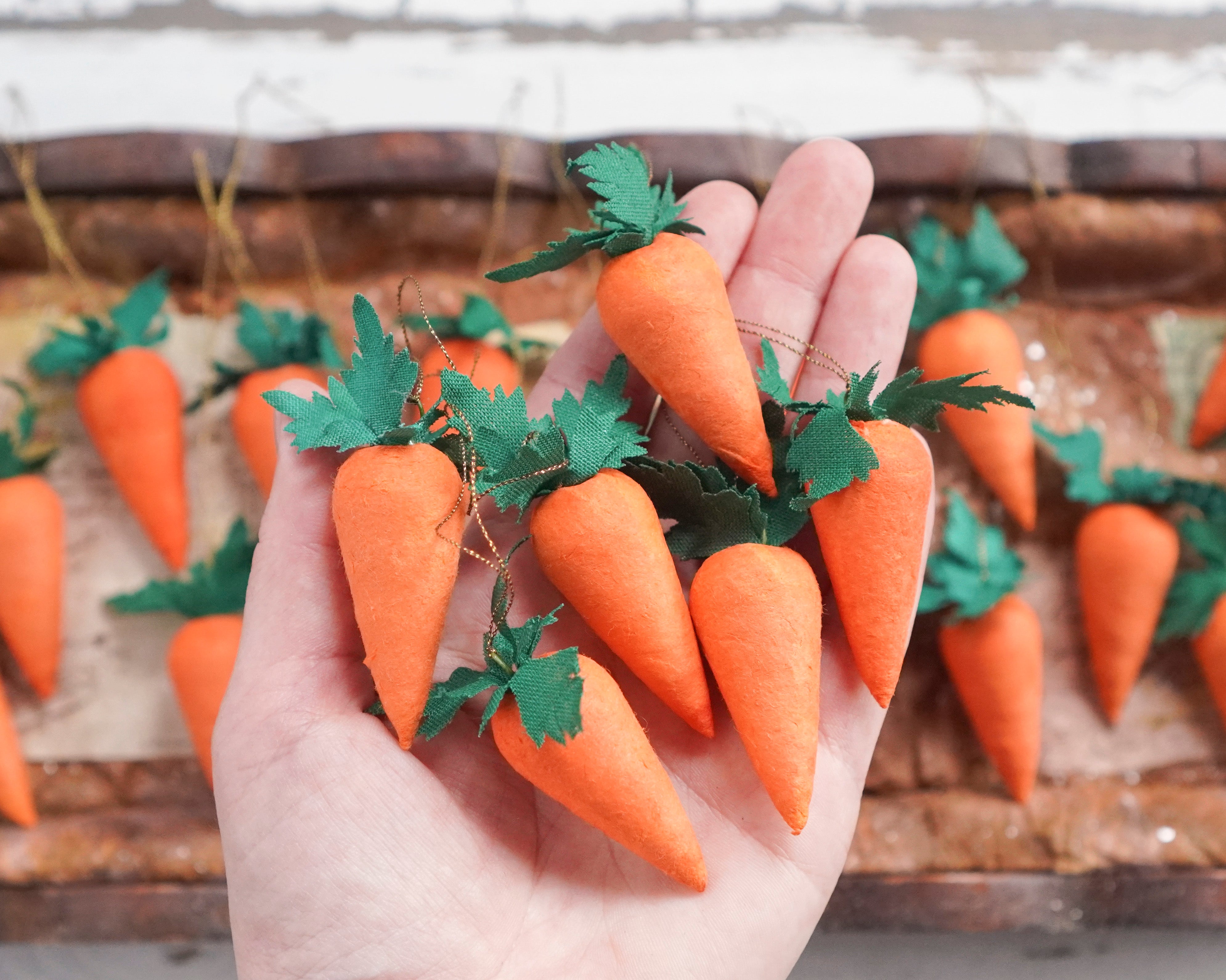 A hand holding a set of six orange spun cotton carrot ornaments with green fabric leaves.