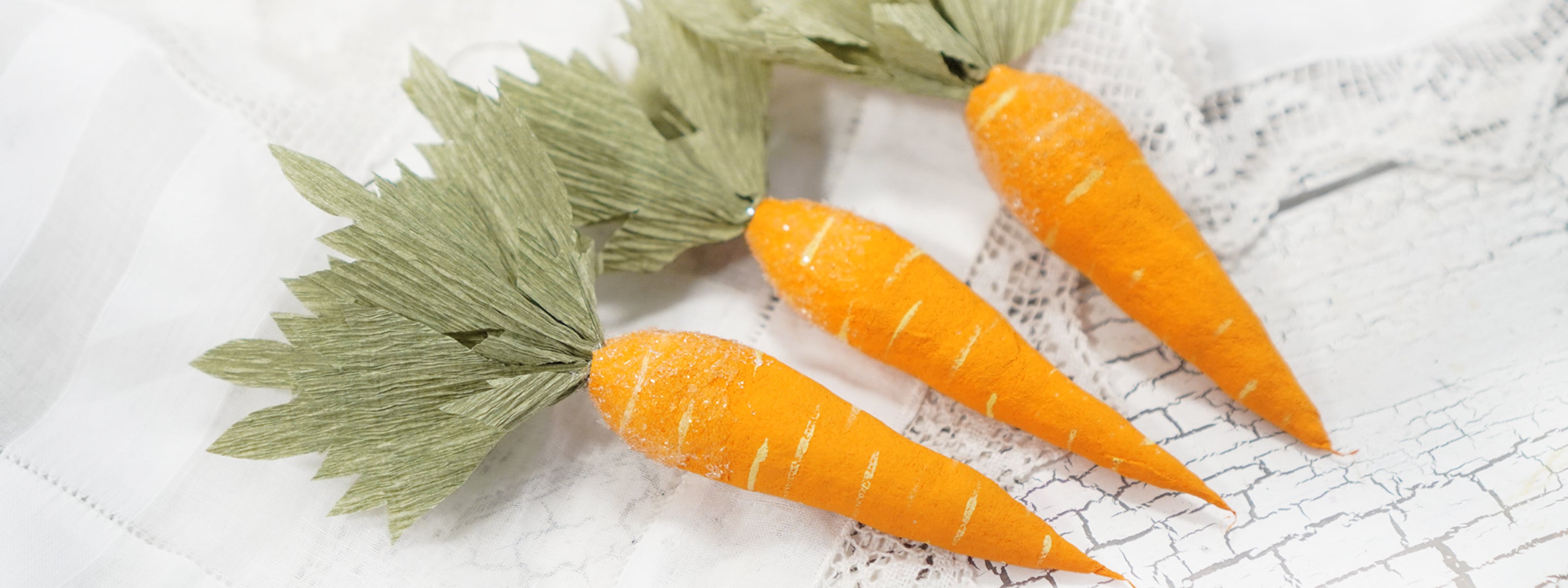 Three spun cotton carrots with green leaves on a textured white surface