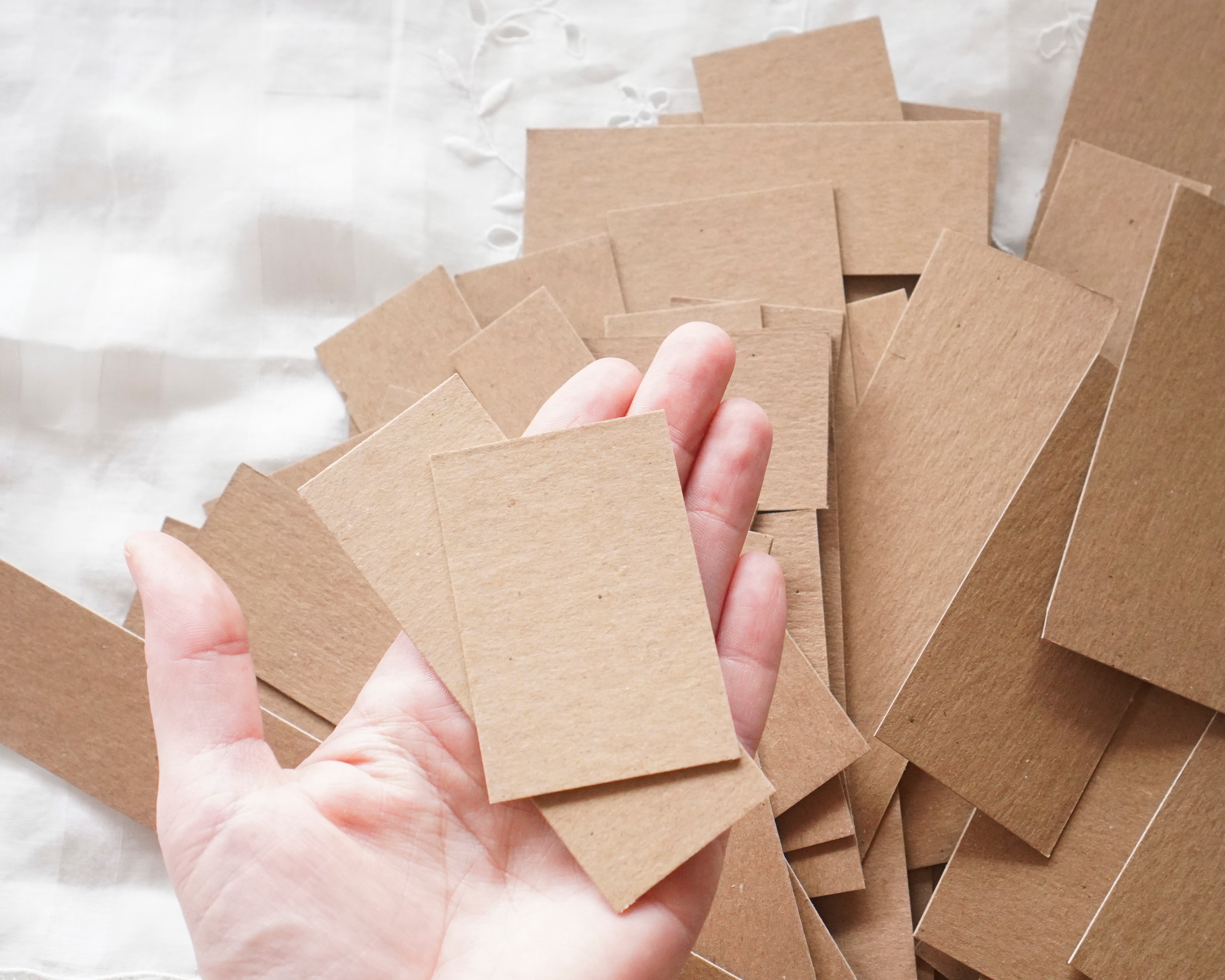 Hand holding a small stack of brown cardboard pieces on a white background