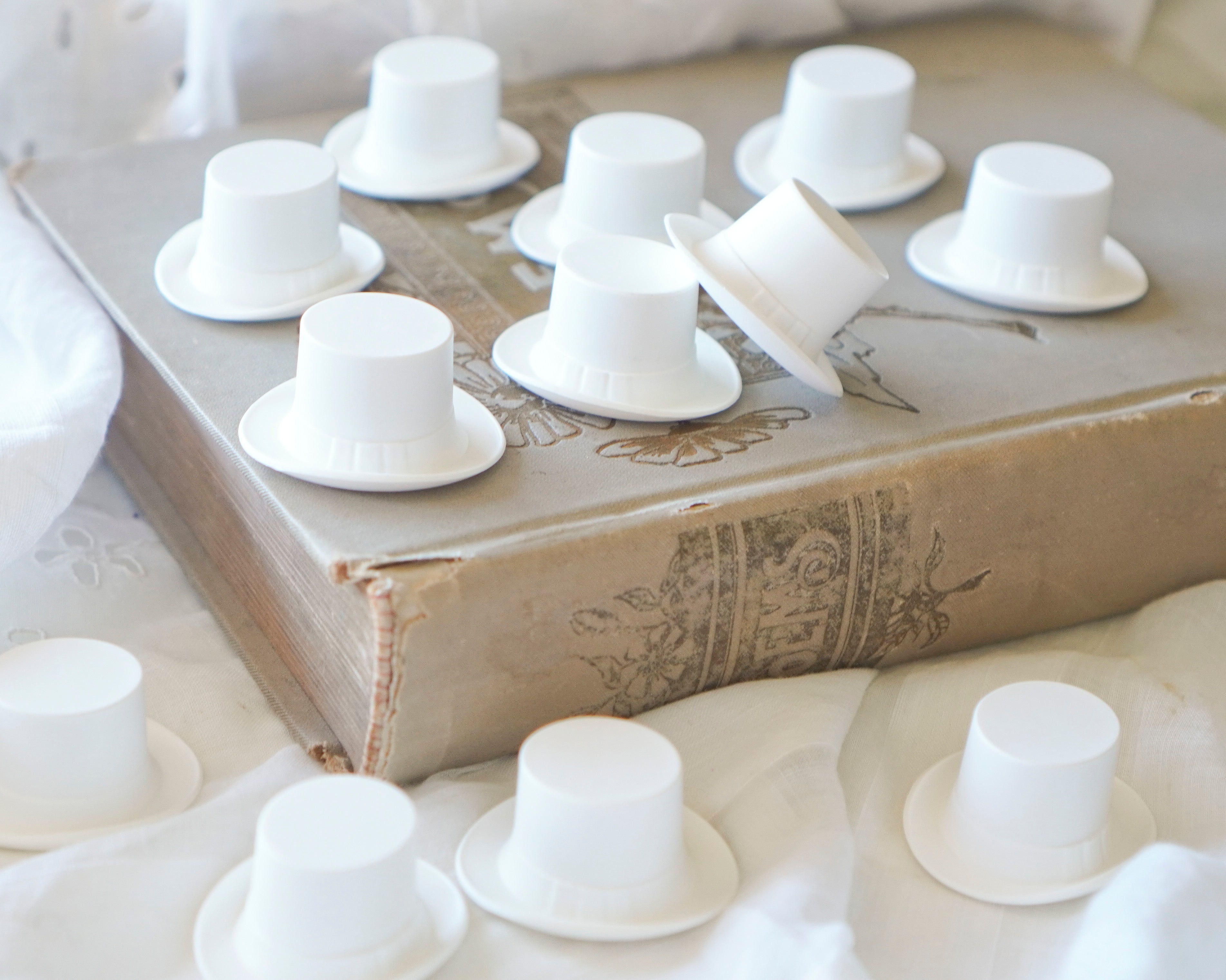 White plastic top hats for dolls on a textured surface with an old book underneath