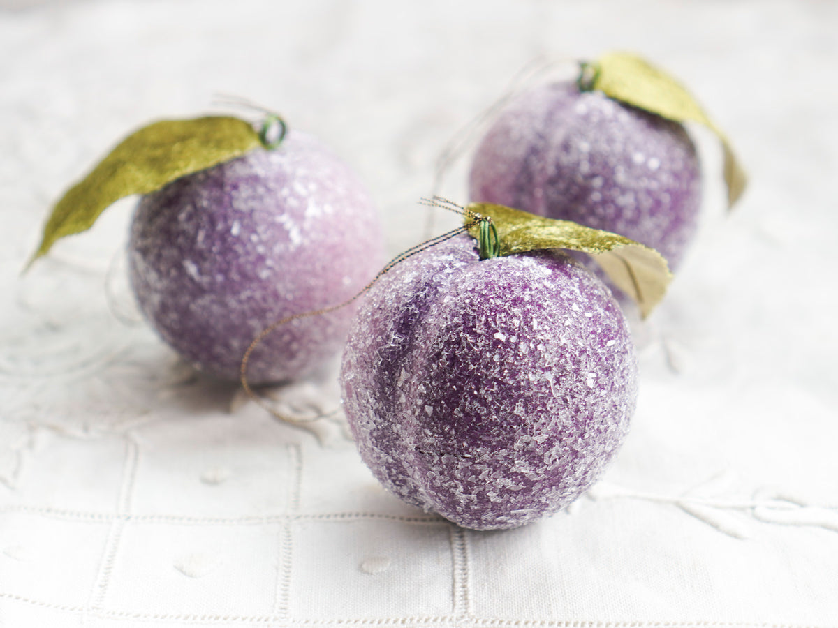 Three spun cotton sugar plum ornaments grouped on a white linen background.