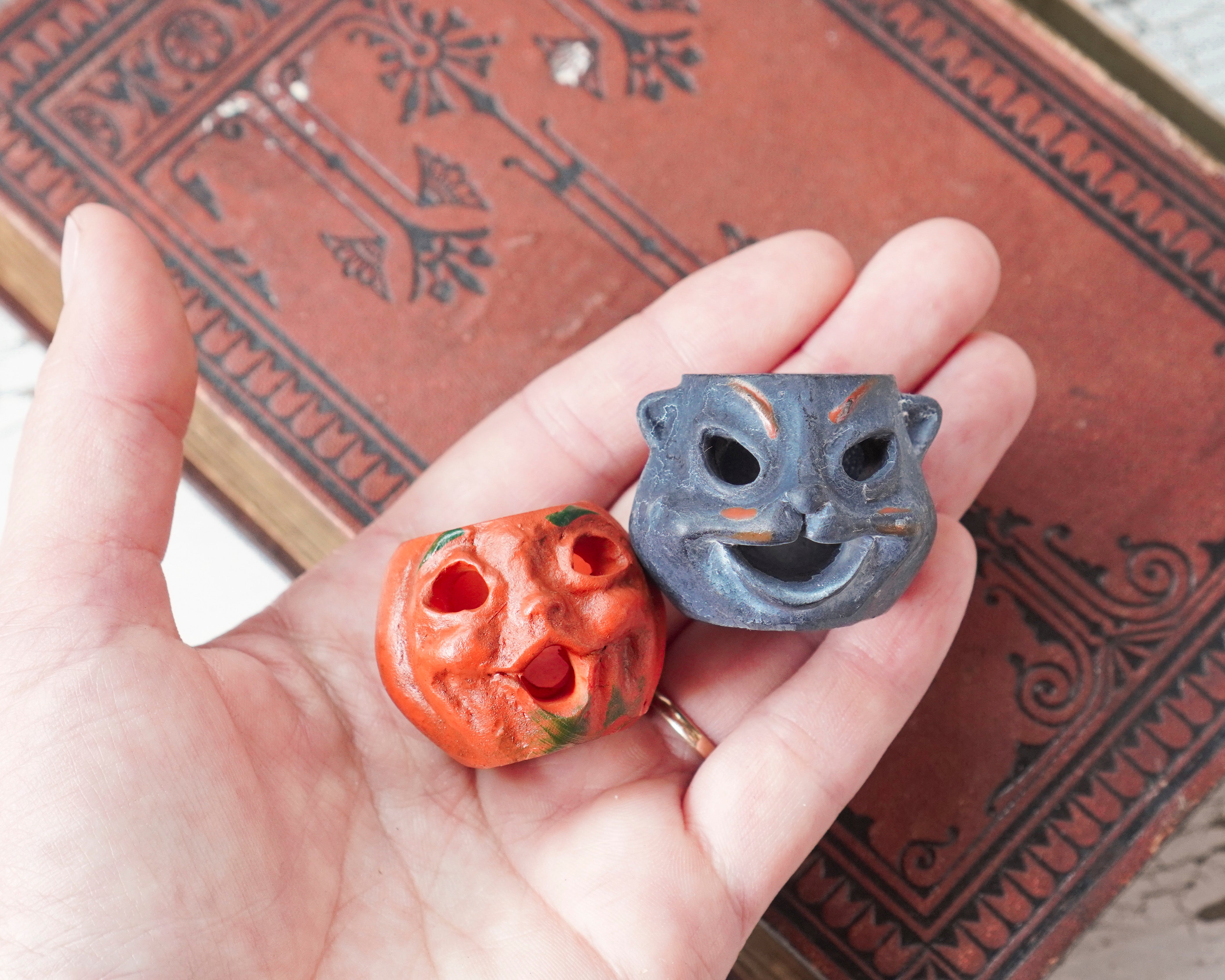 Hand holding two halloween miniatures with faces against a decorative book background