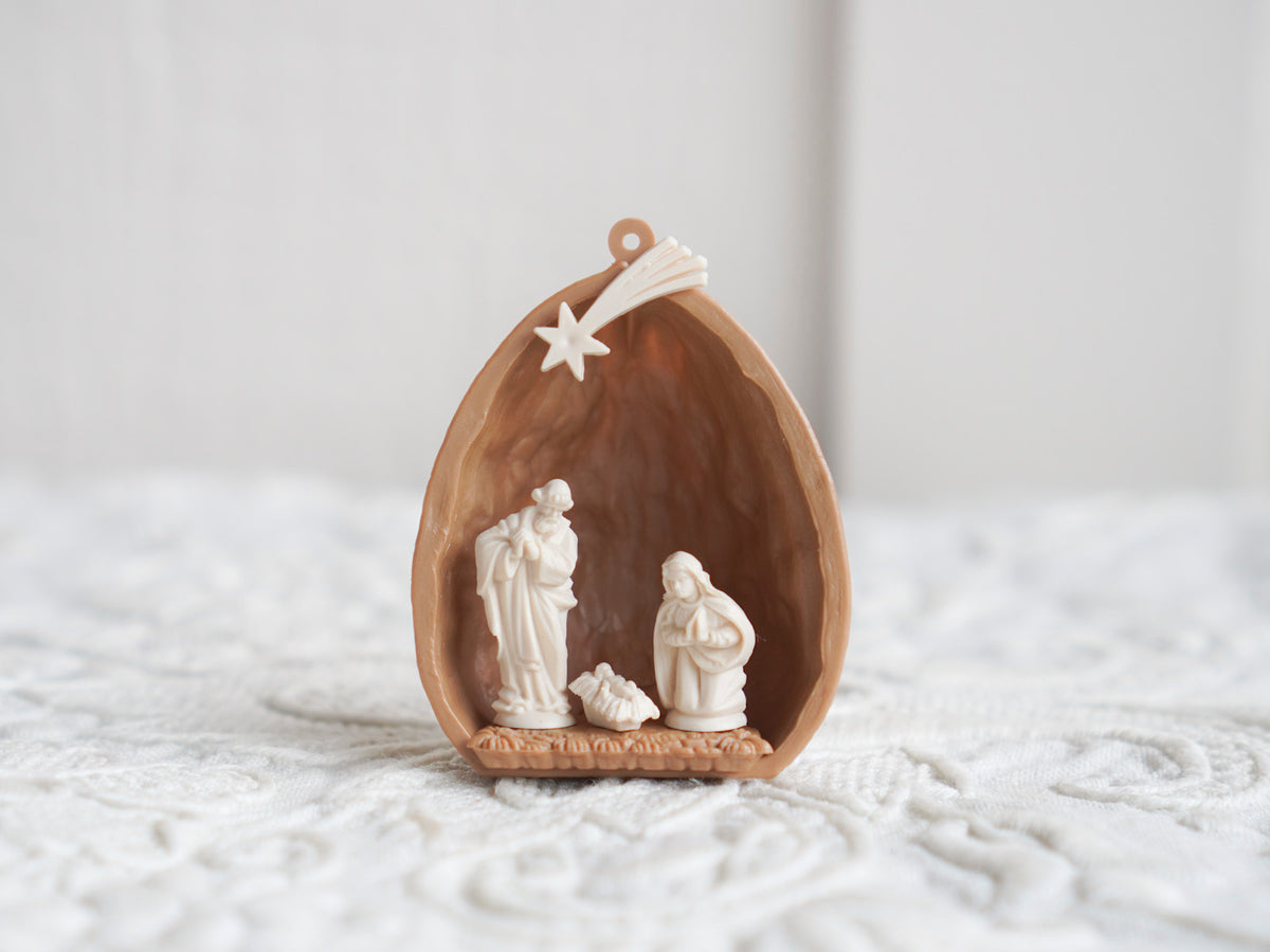 A tiny nativity figure set displayed in a walnut shell on a white background.