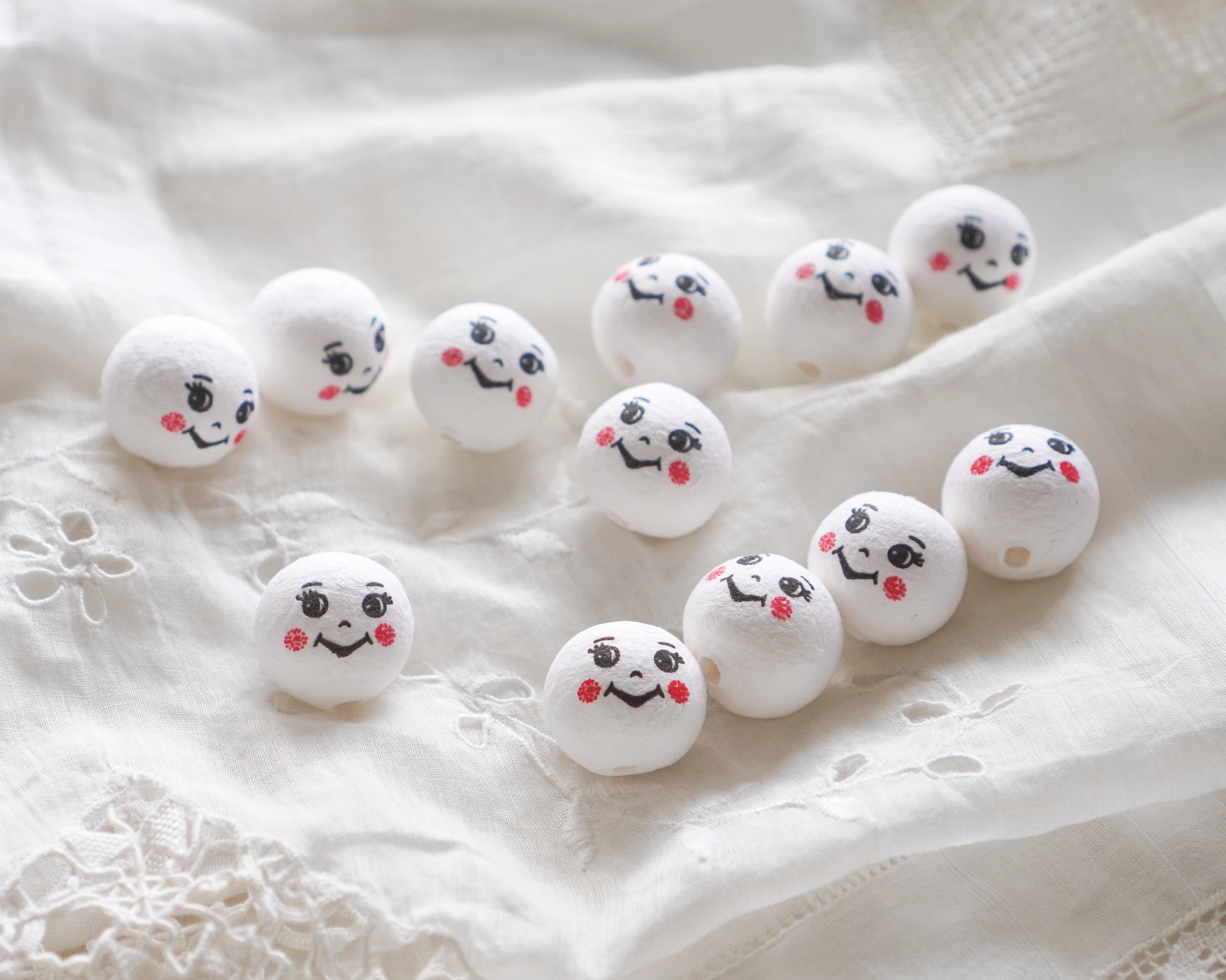 White spun cotton pixie elf heads with smiley face designs on a textured white surface