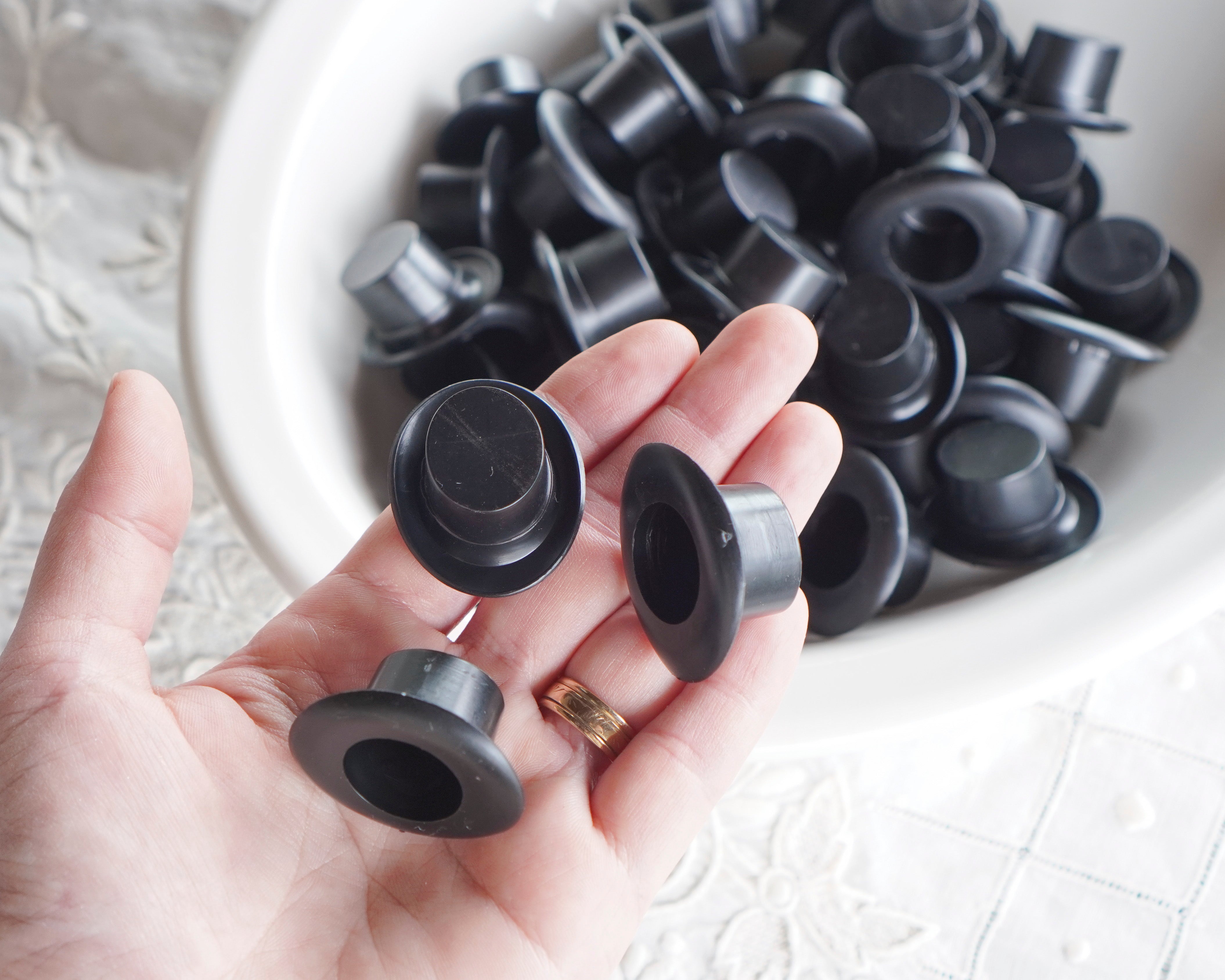 Black plastic craft hats held in a hand with a bowl of more top hats in the background.