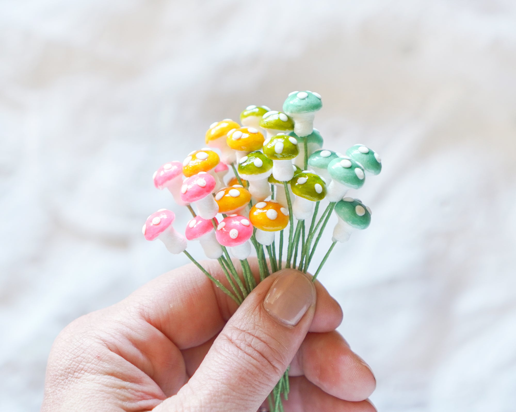 Hand holding small colorful spun cotton mushrooms against a light background