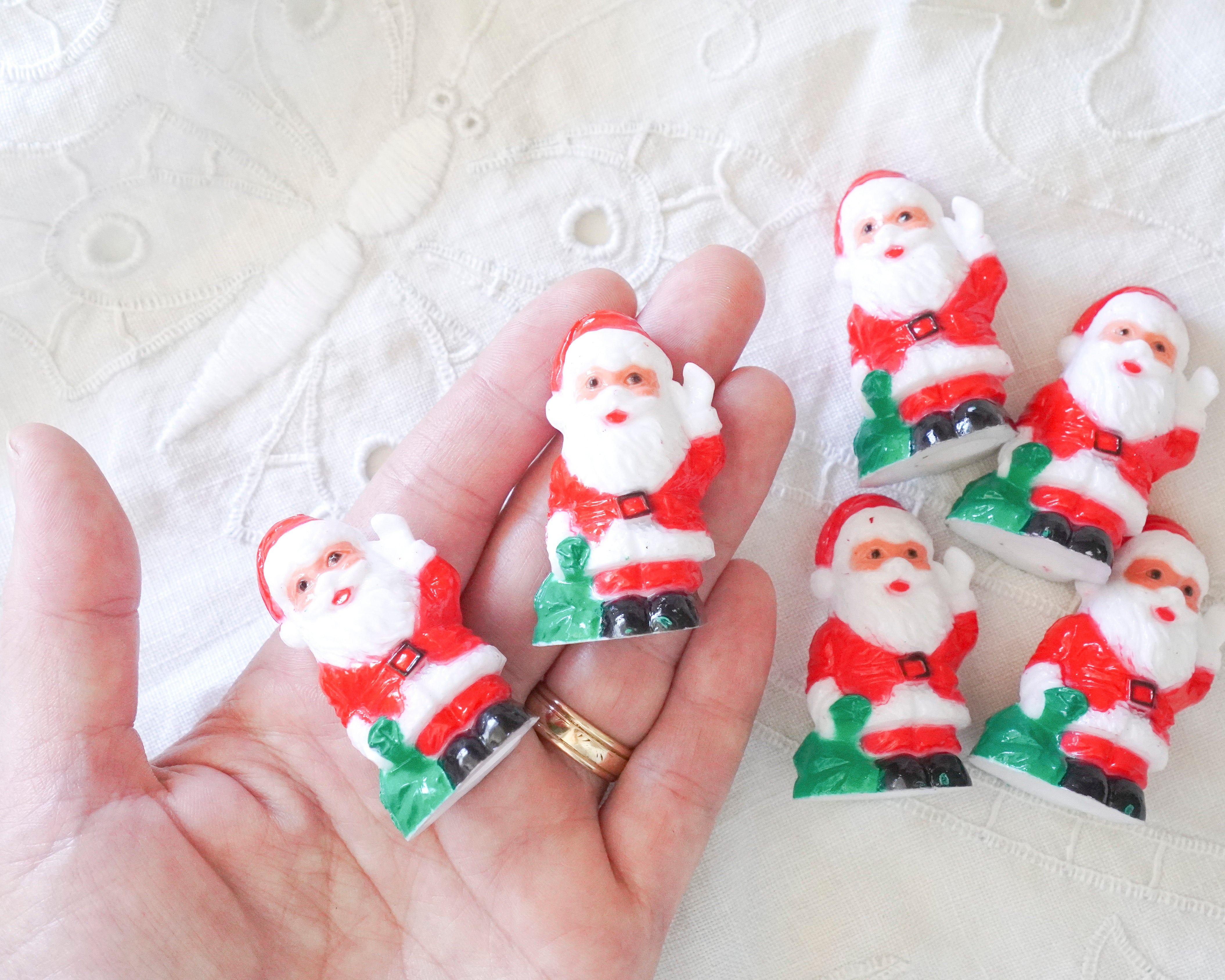 Small Santa Claus figurines held in a hand with a white lace background