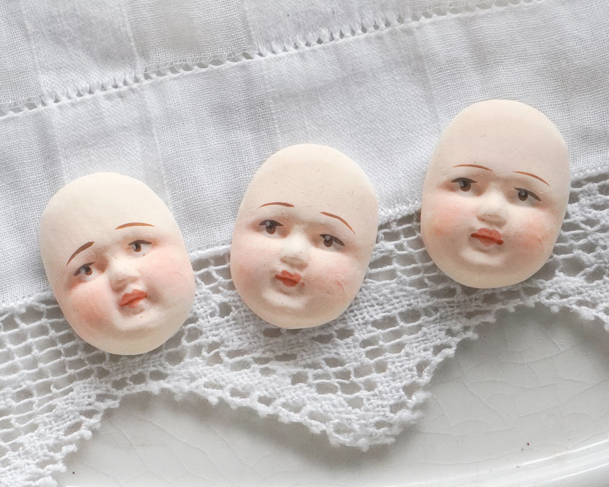 Three vintage style doll heads on a textured white surface