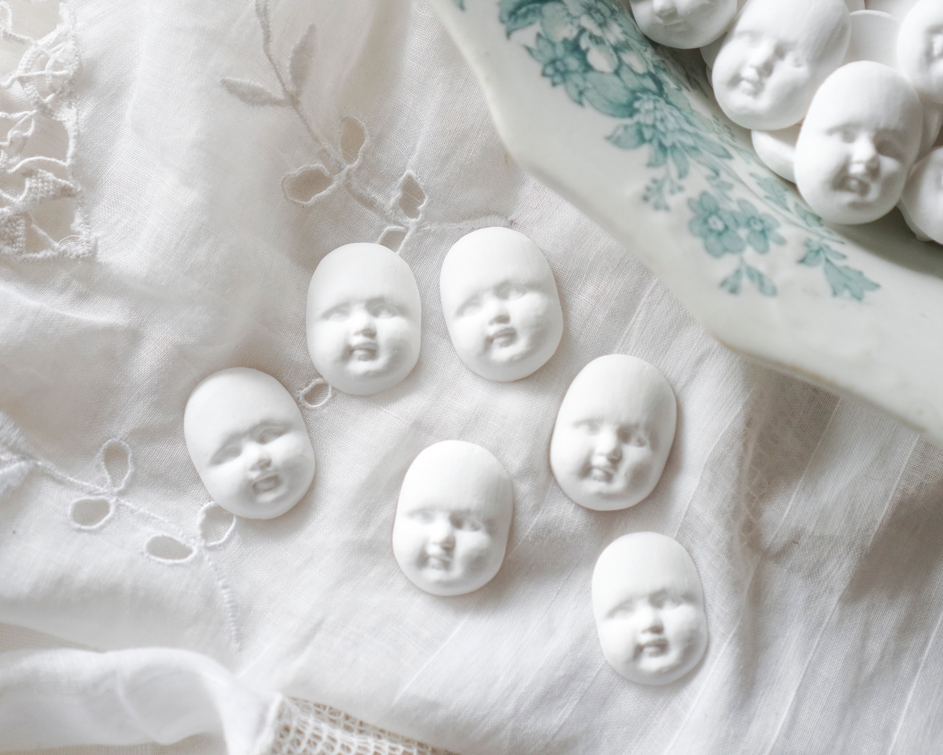 White faux bisque doll heads on a textured white fabric background