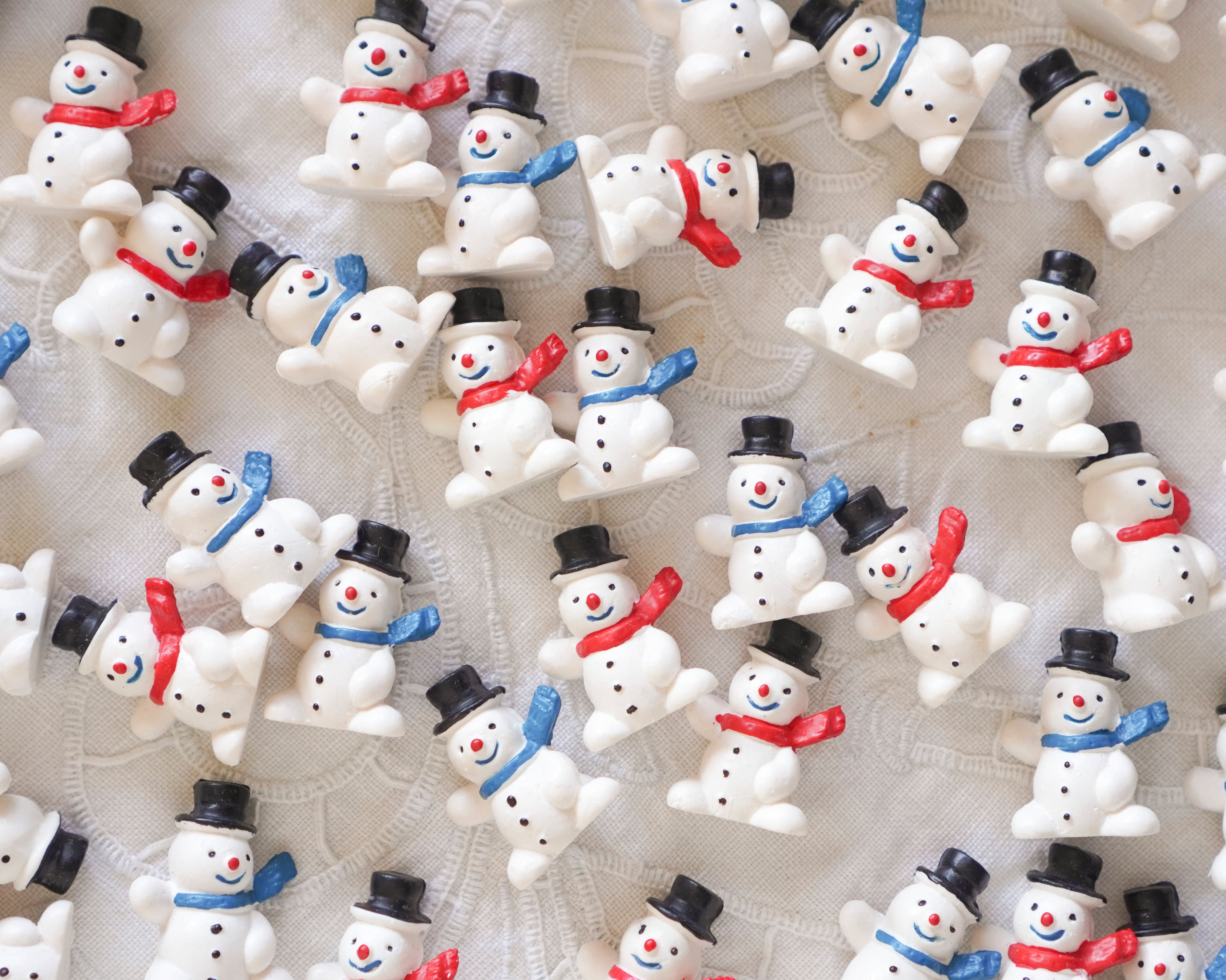 Collection of small snowman figurines with various accessories on a textured white background