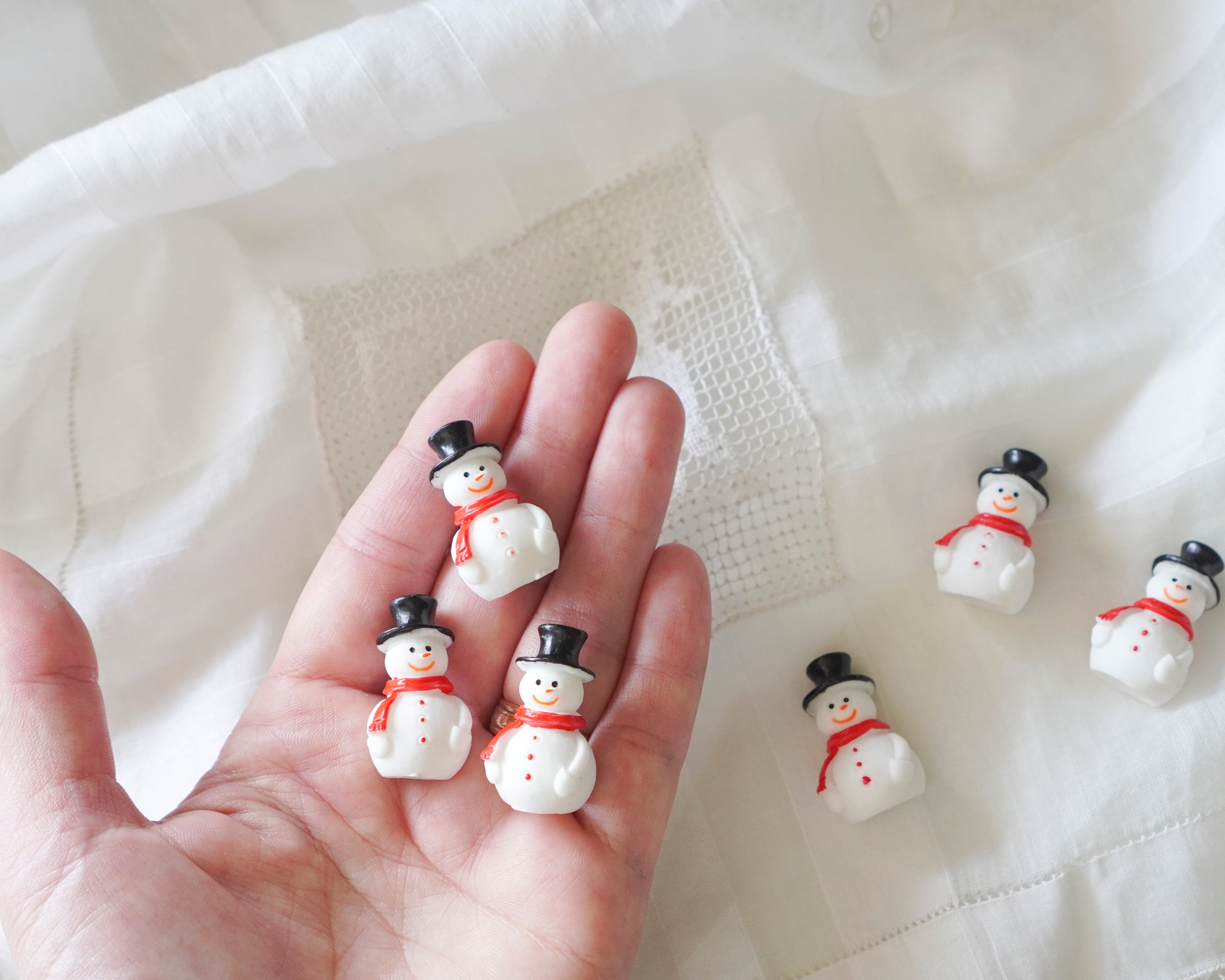 Small snowman figurines held in a hand with a white fabric background