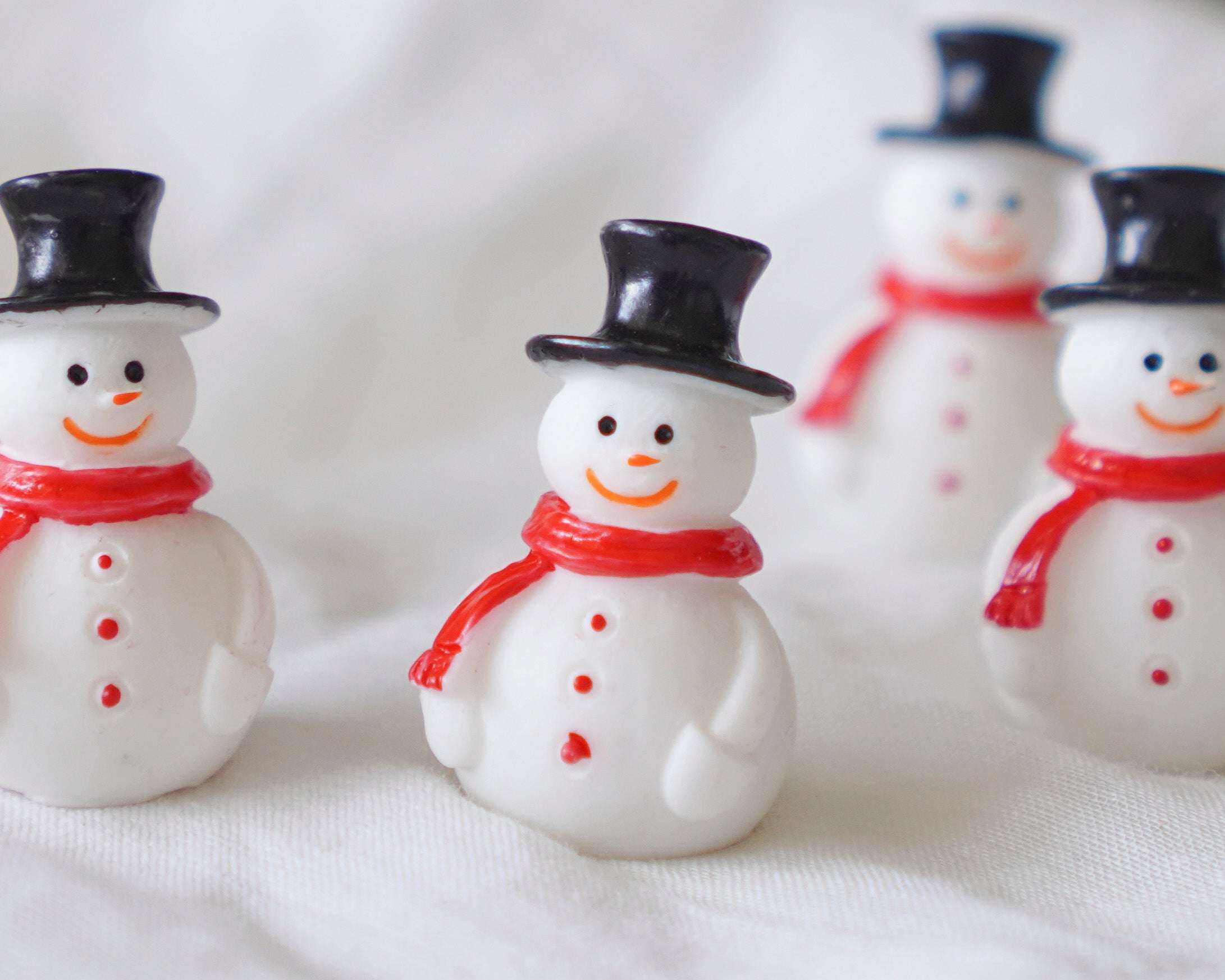 Small snowman figurines with black top hats and red scarves on a white background