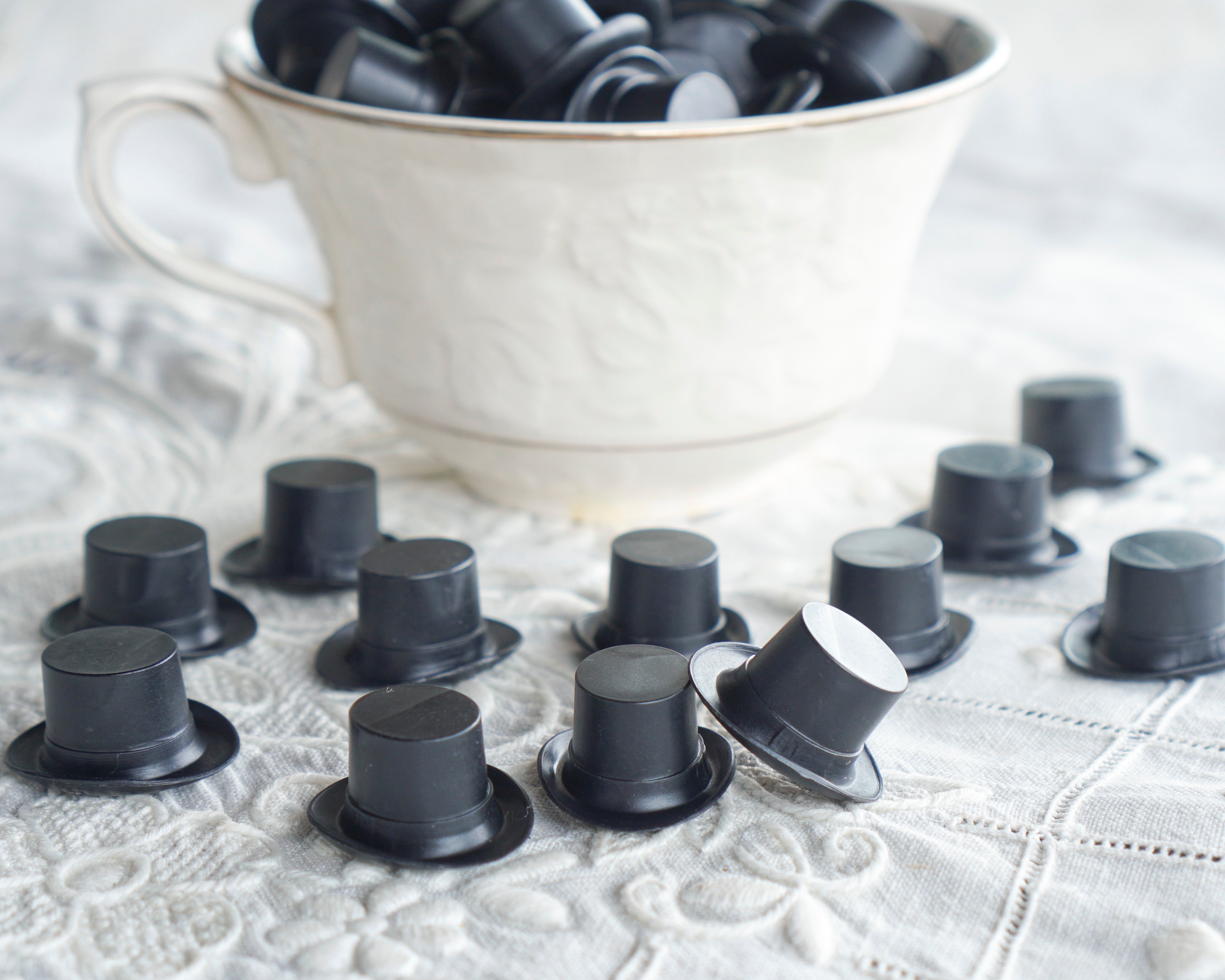Black craft top hats scattered on a textured surface with a white teacup in the background.