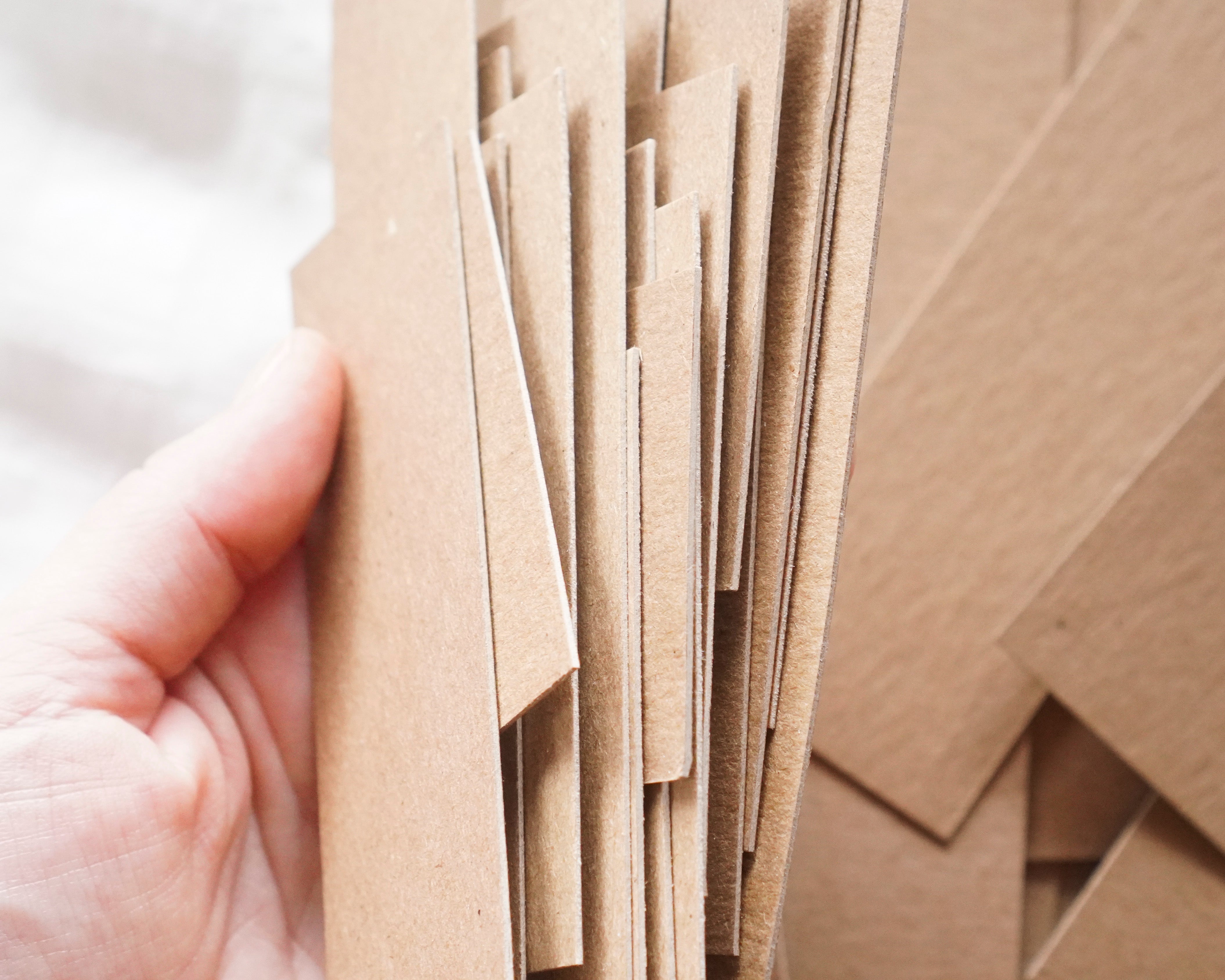 Hand holding a stack of brown chipboard sheets