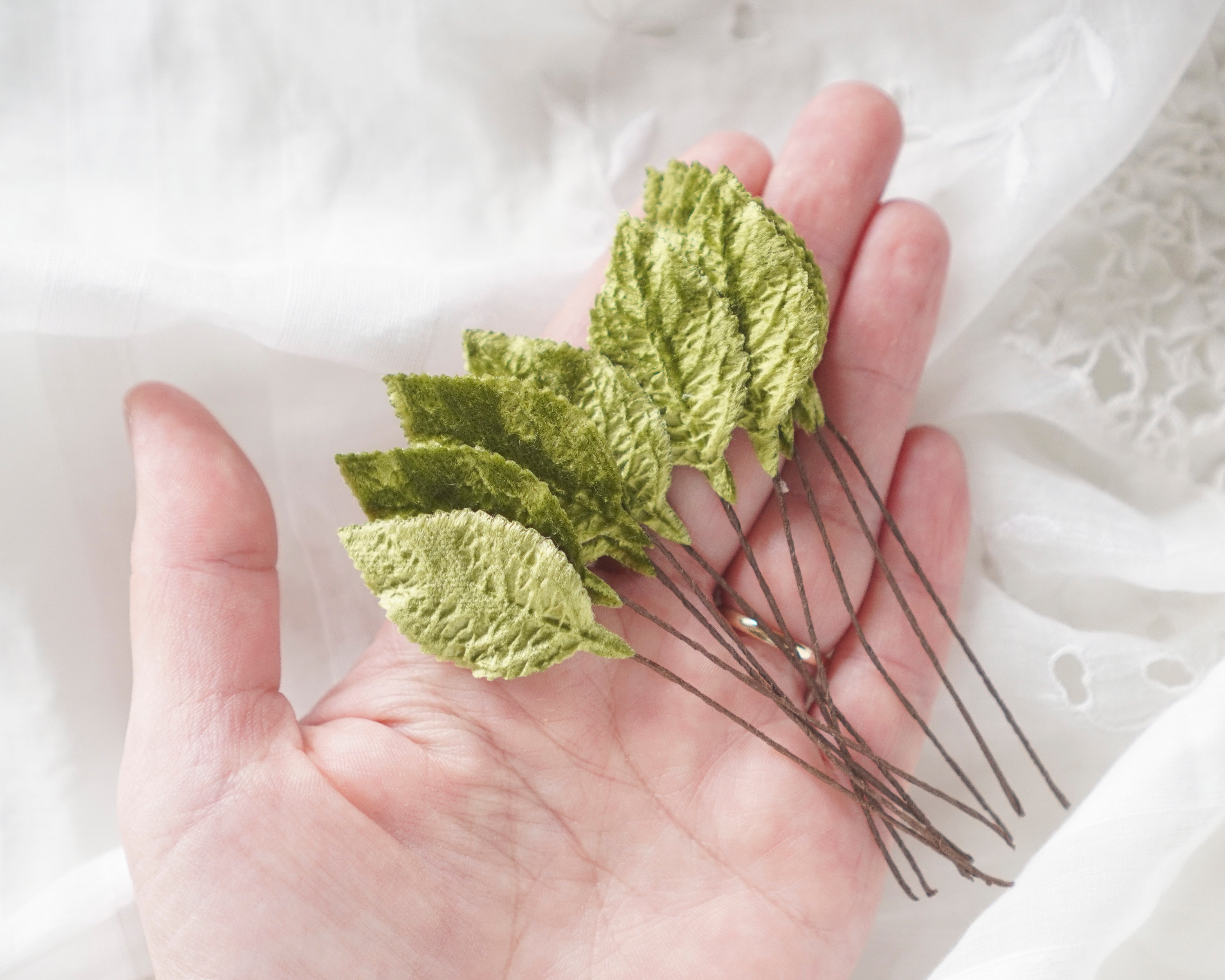 Hand holding green velvet leaves with stems against a white lace background