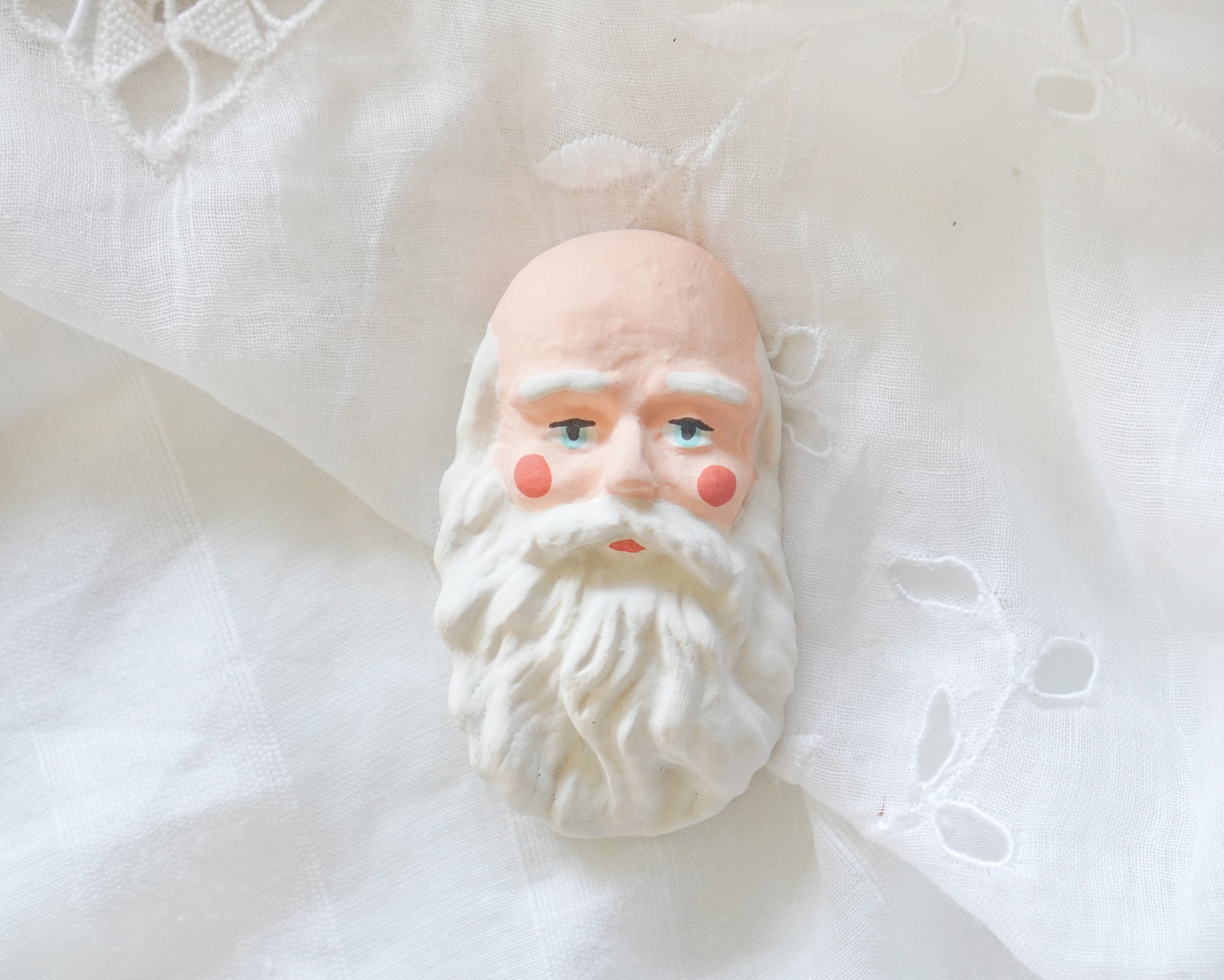 An old fashioned Father Christmas doll face on a white lace background.