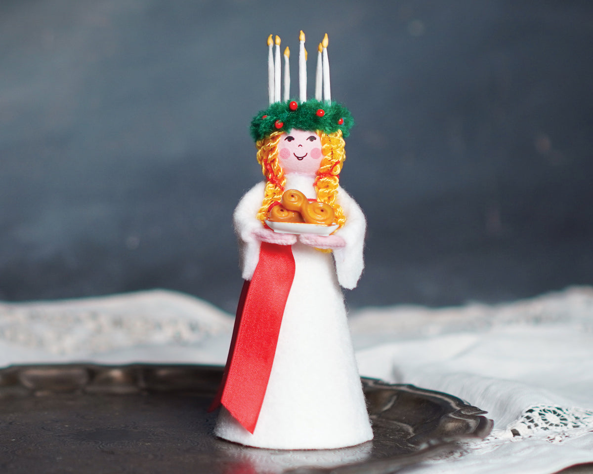 A small figure of Saint Lucy set on a plate in front of a gray background.
