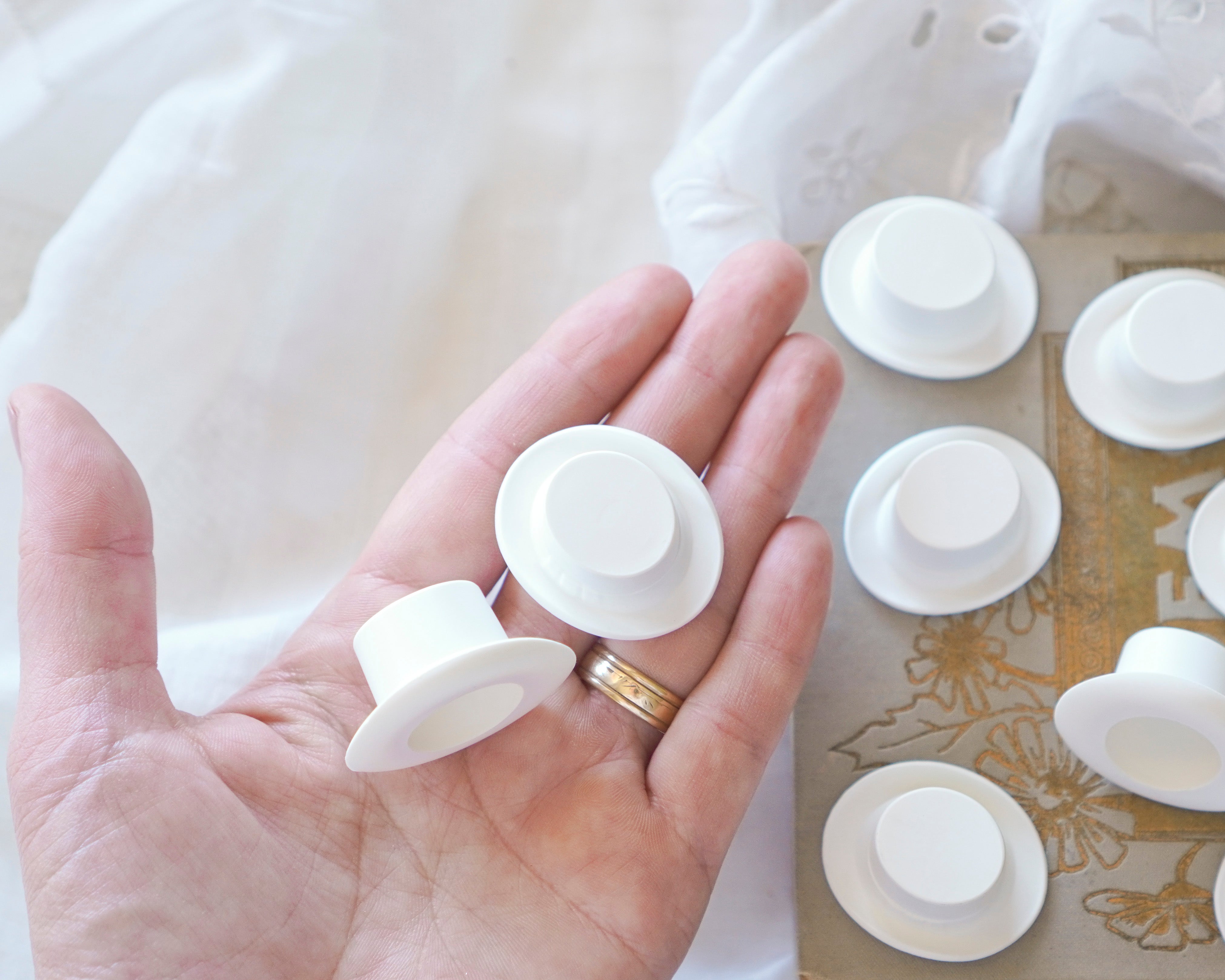 Hand holding white craft top hats with more objects in the background