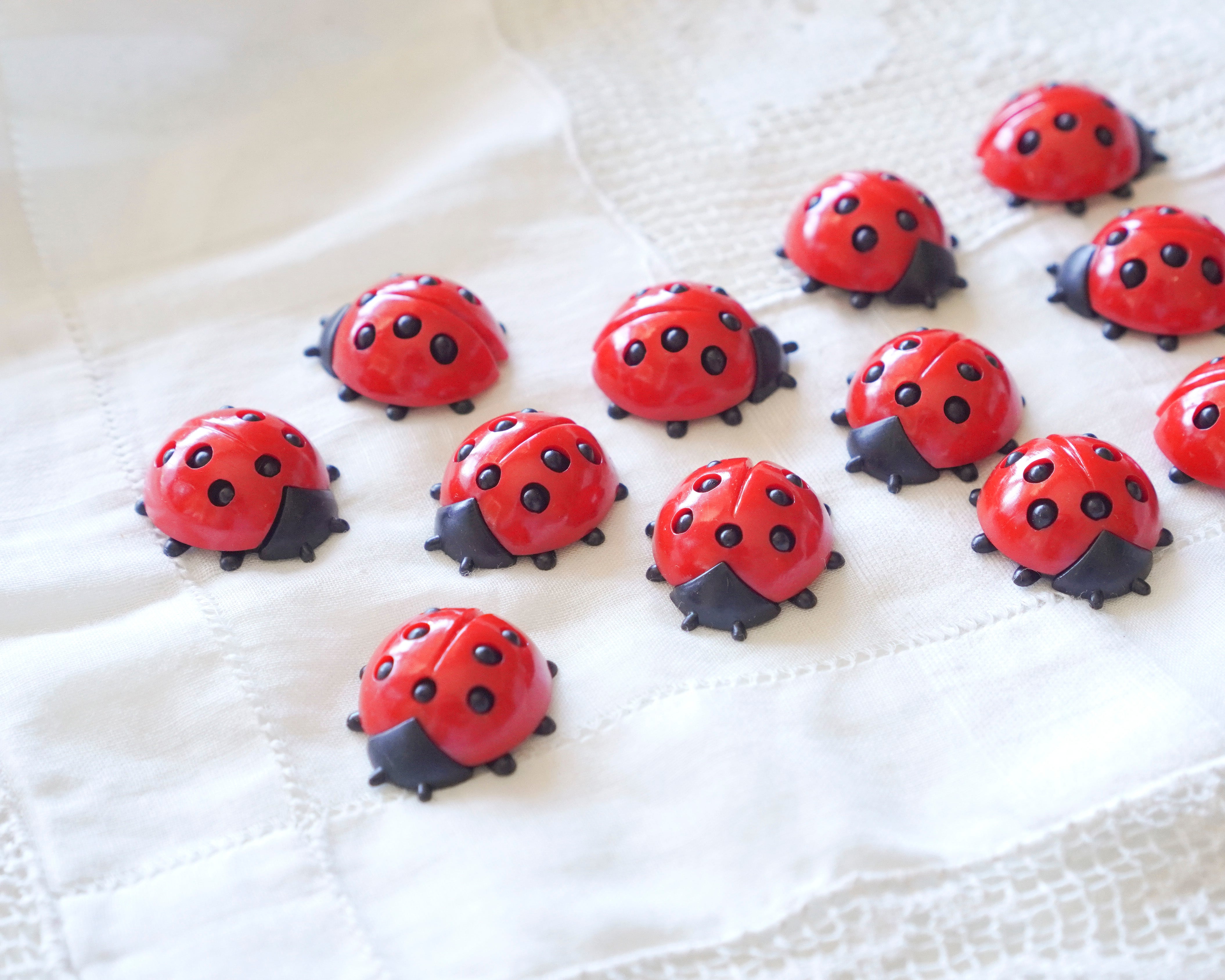 Red ladybug-shaped craft embellishments on a white lace fabric background