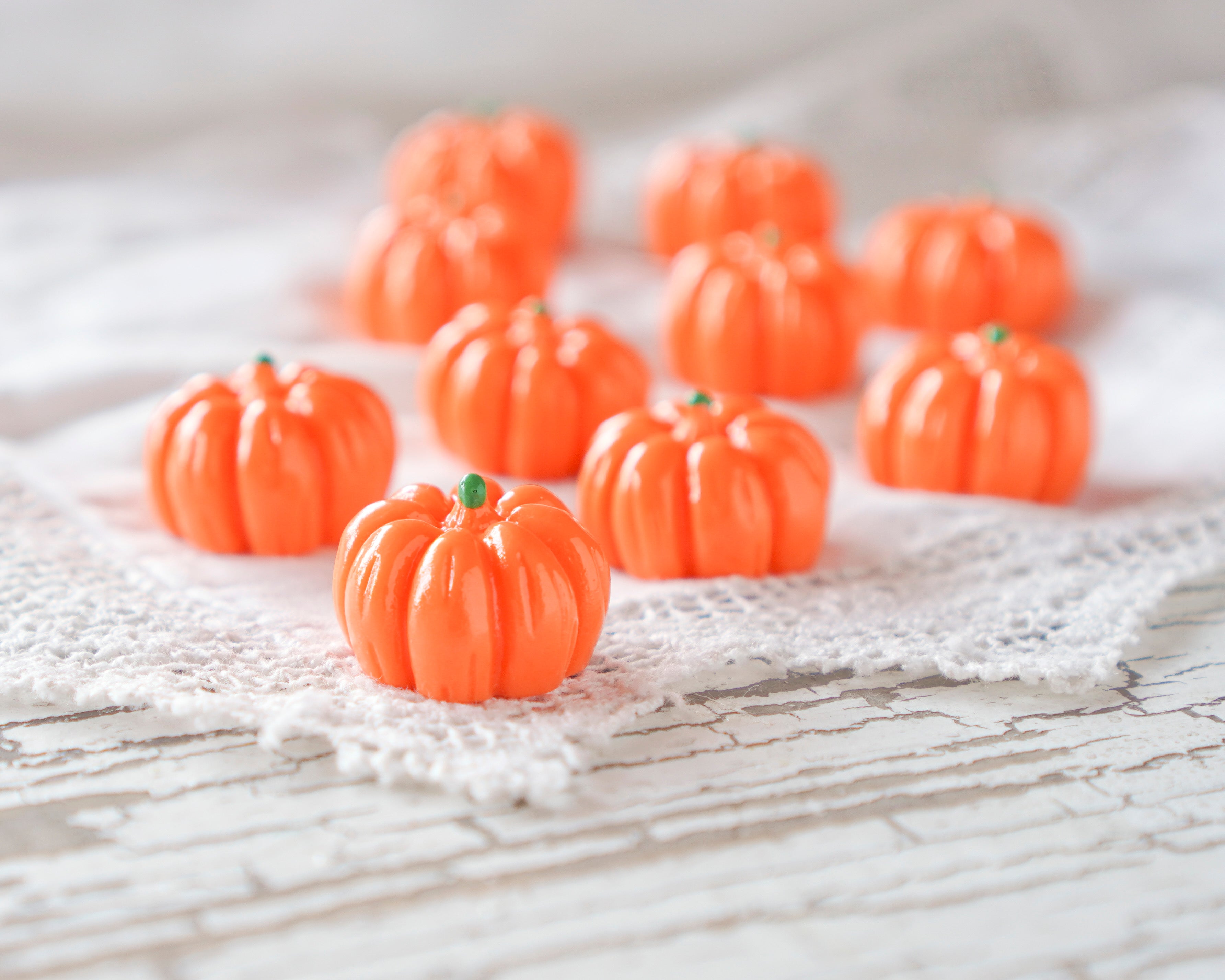 Several small orange pumpkins arranged on a white lace cloth over a white wooden surface.