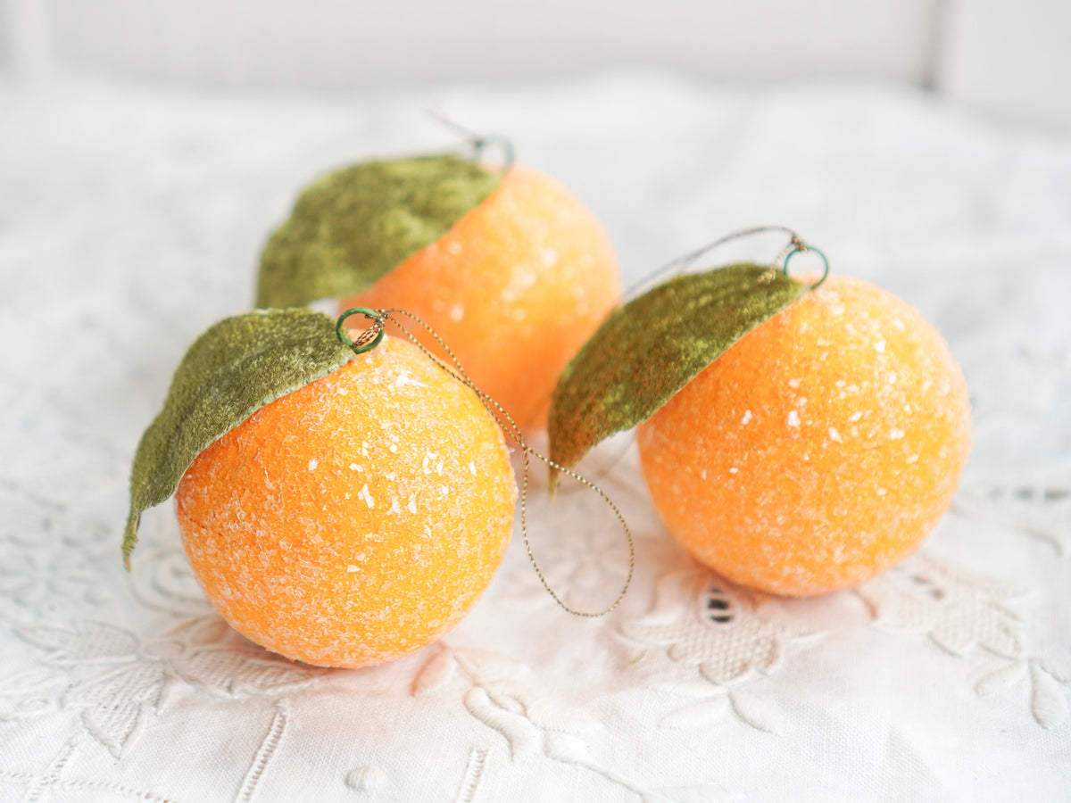 Three spun cotton sugared fruit ornaments grouped on a white linen background.